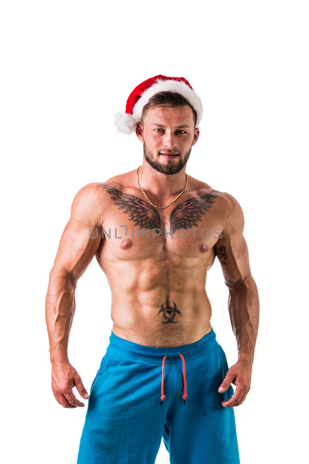 Christmas season: muscular bodybuilder shirtless wearing Santa Claus red hat, isolated on white