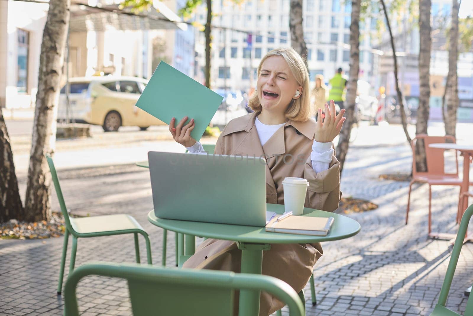 Portrait of upset, crying young woman, sitting with laptop, sobbing from failure and disappointment, failing something, having mental breakdown on street. Lifestyle and emotions concept