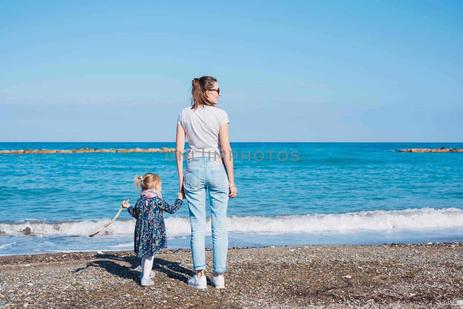 Back view of mother and her little daughter looking at the sea