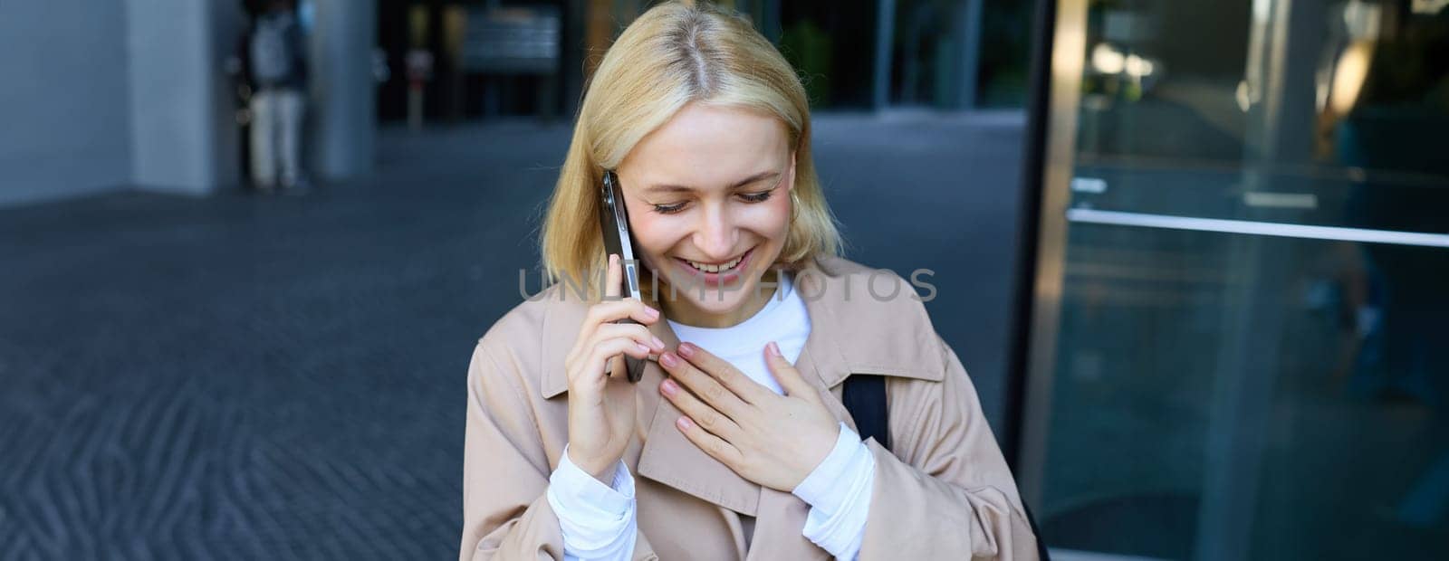 Close up portrait of smiling, laughing young woman, talking on mobile phone, standing outdoors, walking on street with smartphone and chatting by Benzoix