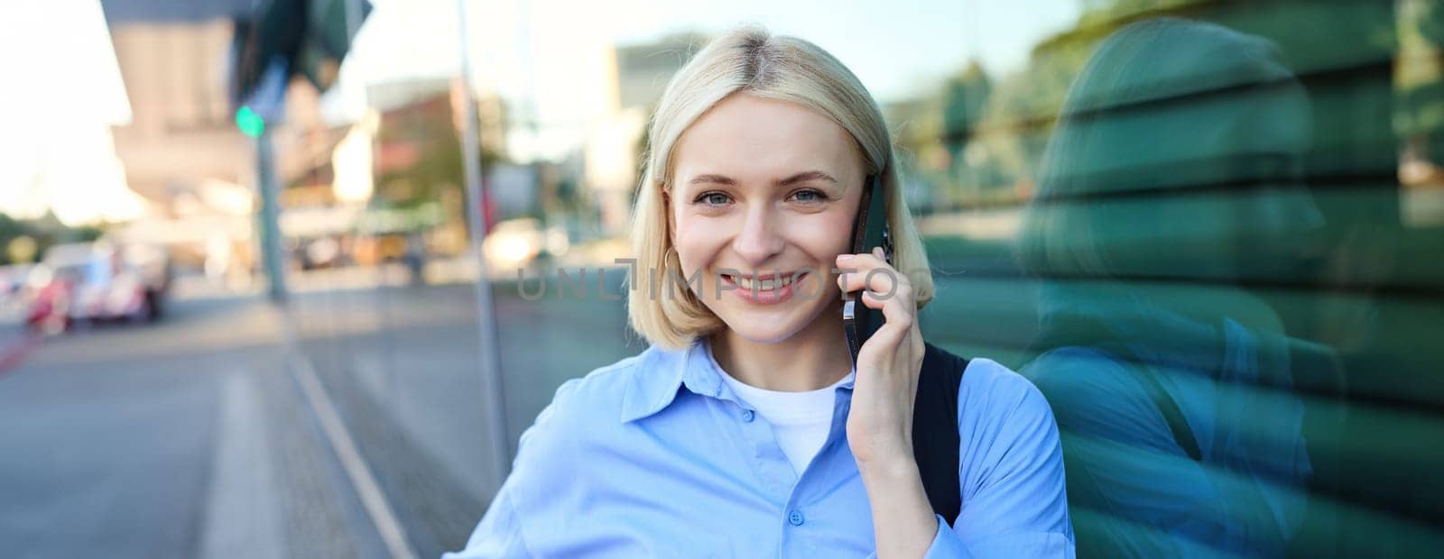 Close up portrait of smiling blond woman, chatting on the phone, talking on mobile telephone, standing on street outdoors by Benzoix