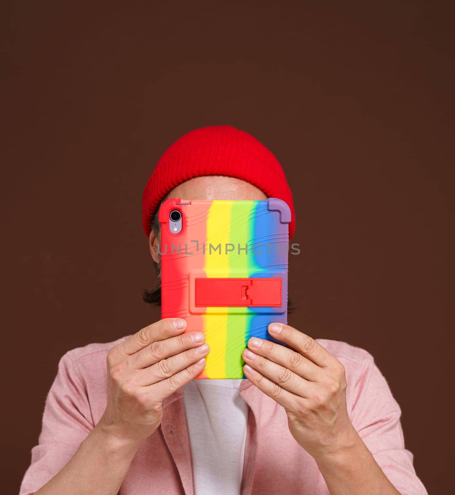 Anonymous person conceals face over tablet PC with LGBT gay rainbow colors. Intersection of digital identity and LGBTQ pride, emphasizing need for privacy and protection in digital space of gay pride movement. High quality photo