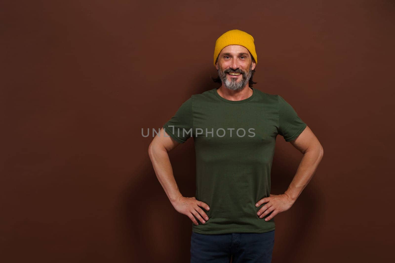Happy confident middle-aged man standing with hands on sides on brown background. Posture and joyful smile convey sense of confidence, contentment, and success. mature individual in assertive stance. High quality photo