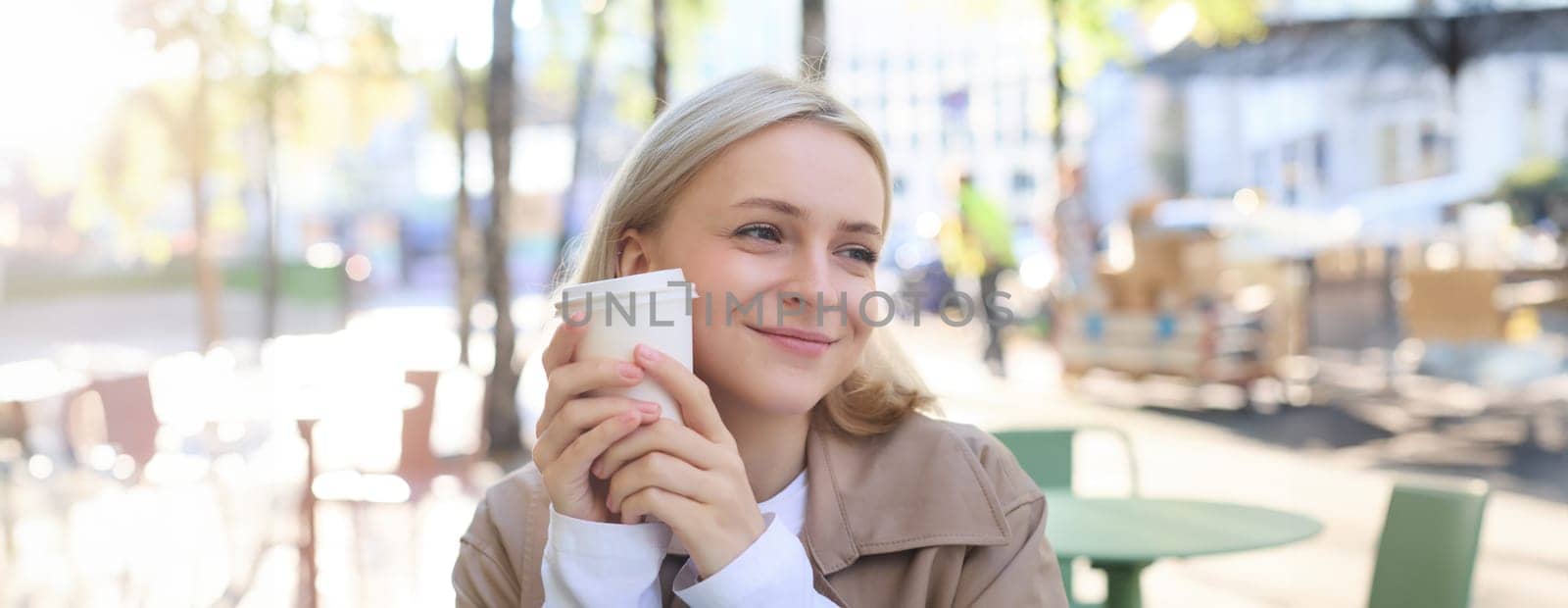 Close up portrait of smiling, happy beautiful European woman, sitting in cafe and enjoying cup of coffee, drinking beverage, enjoying bright sunny day outdoors.