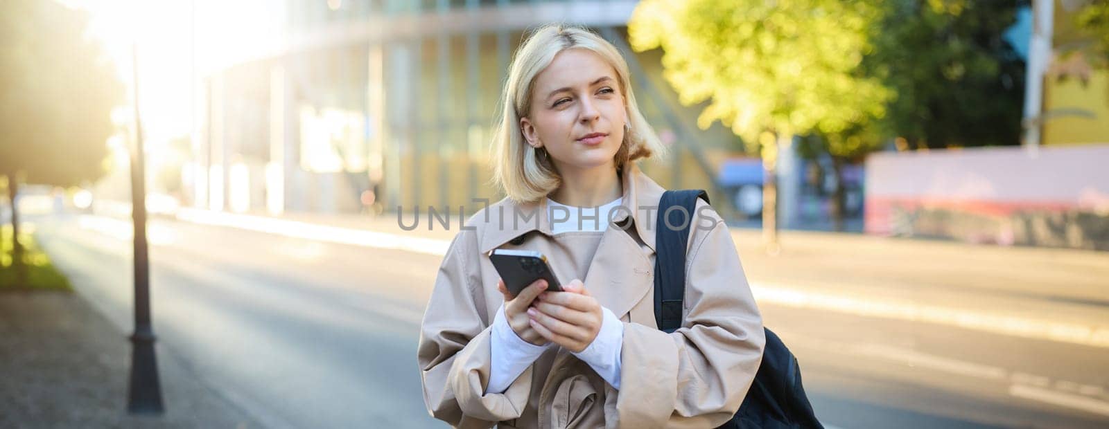 Portrait of woman thinking, calculating in her head, standing on street with smartphone, using mobile phone map application while exploring the city.