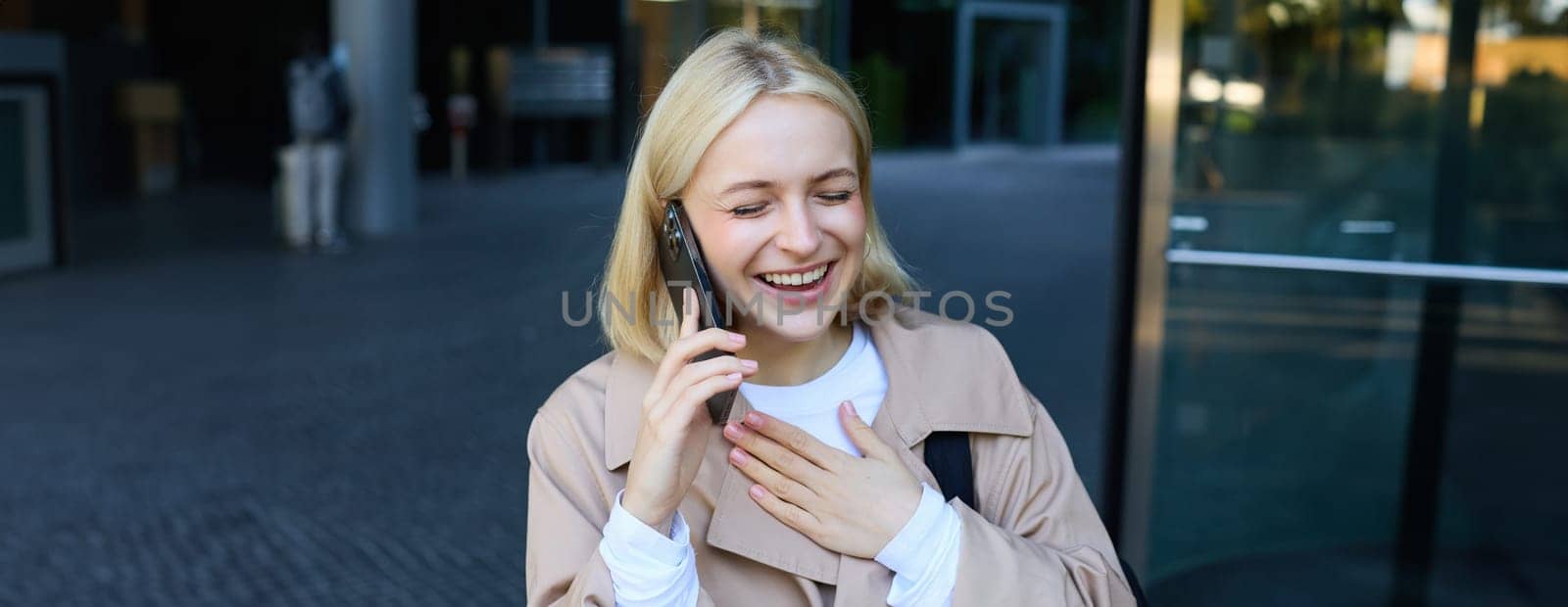 Close up portrait of carefree blond woman, talking on mobile phone, answer a call, laughing over funny conversation on smartphone.