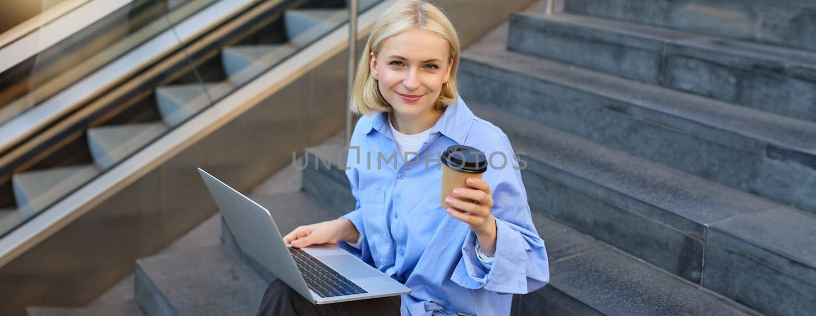 Image of stylish young woman, college student with laptop, sitting on city stairs and drinking coffee, working on project, studying outdoors, connects to public wifi, enjoying weather by Benzoix