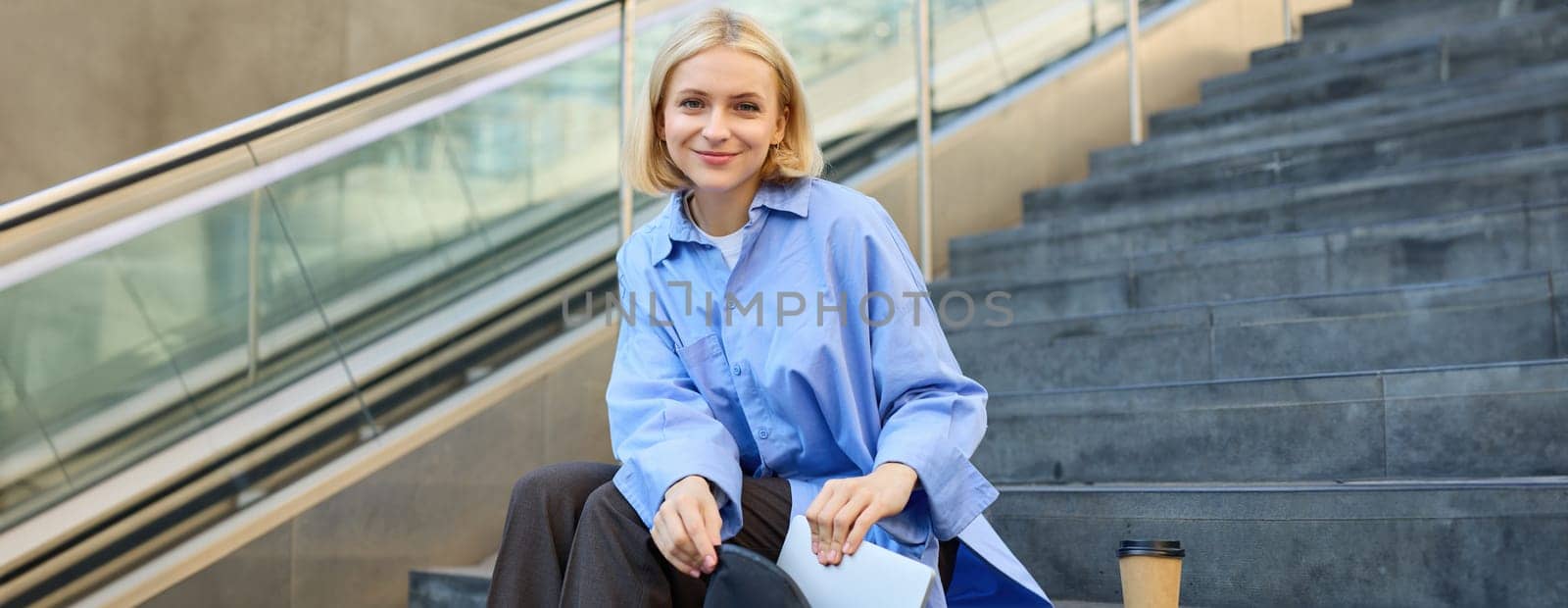 Young woman sitting on street stairs, packing her things, laptop inside backpack pocket, getting ready to go, spending time outdoors by Benzoix