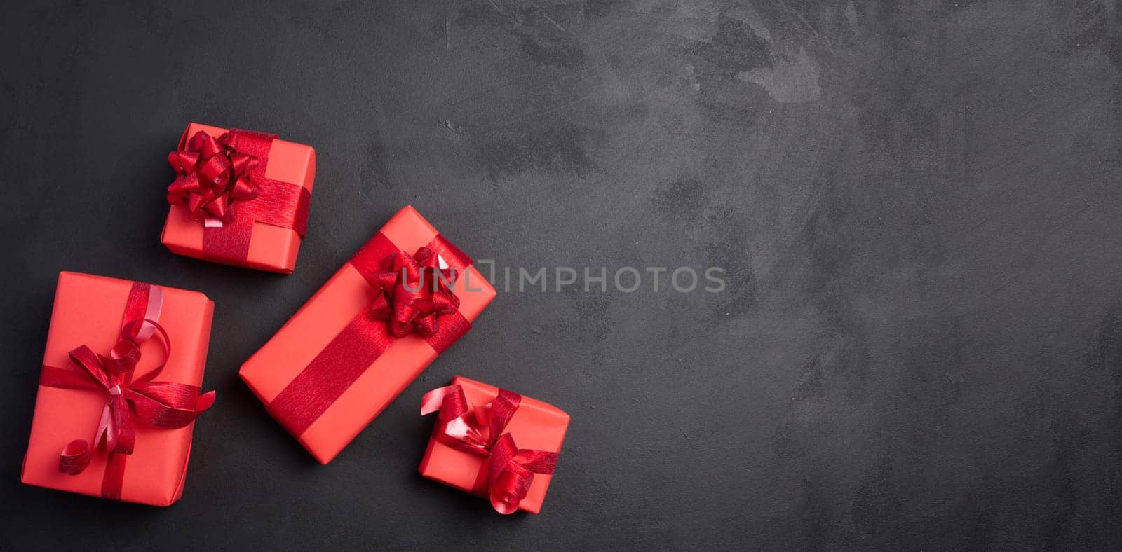 Boxes packed in red paper and tied with ribbon on a black background, gifts. Copy space