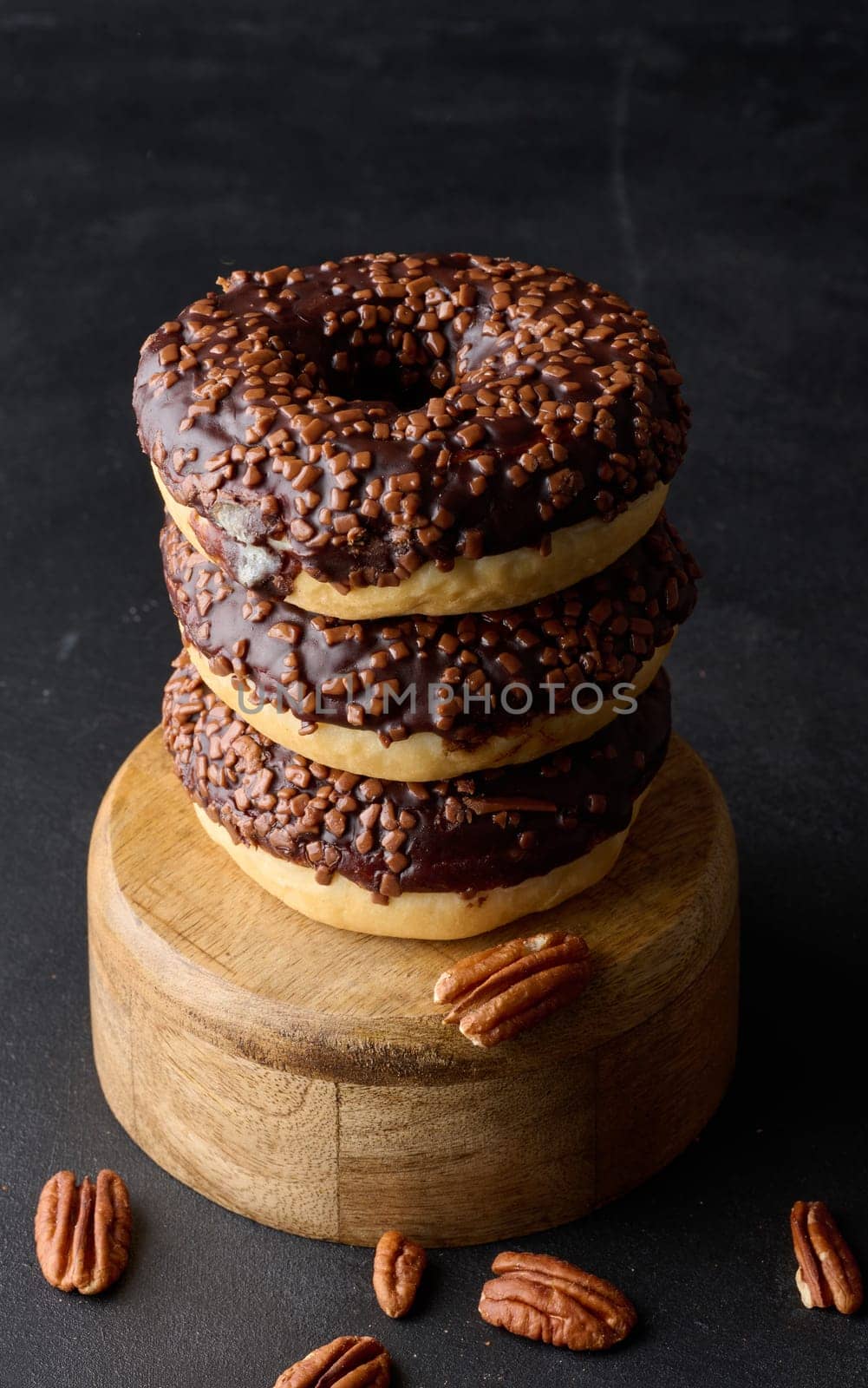 Chocolate donuts sprinkled with crushed nuts on a black table by ndanko