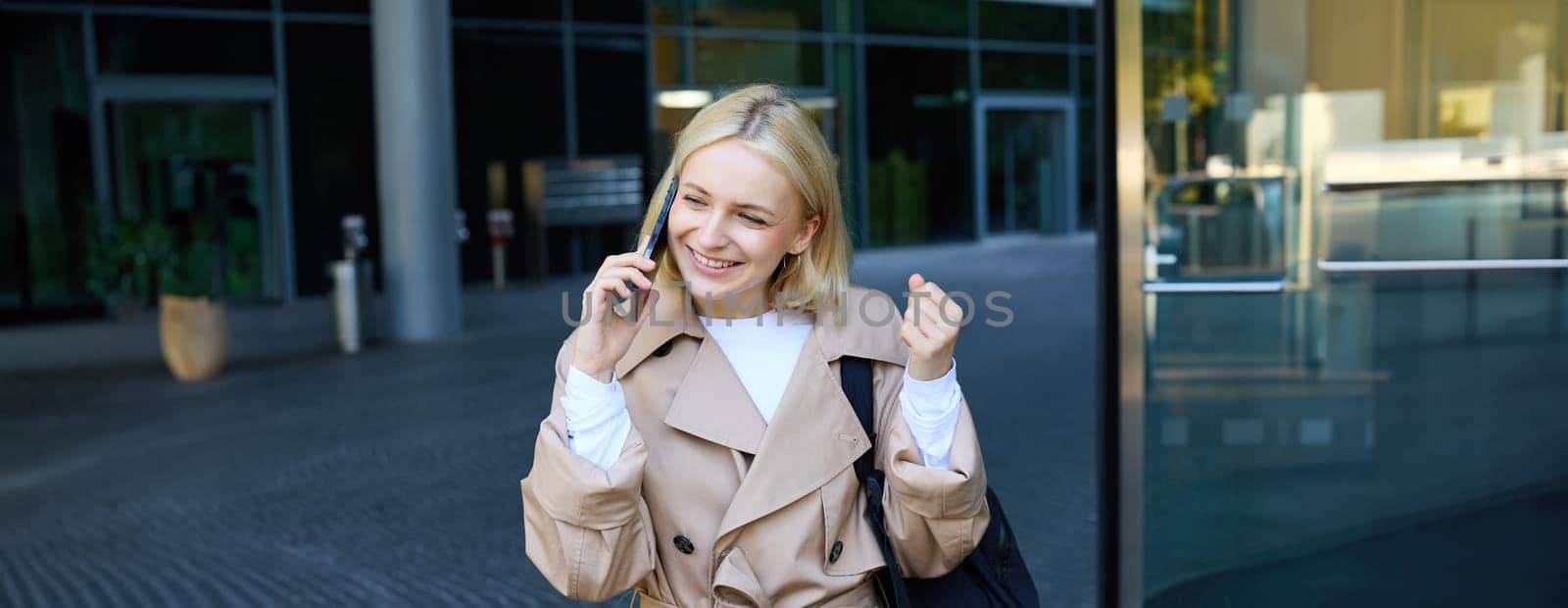 Close up portrait of young blond woman, walking on street and talking on mobile phone, chatting with friend on smartphone. Lifestyle and people concept