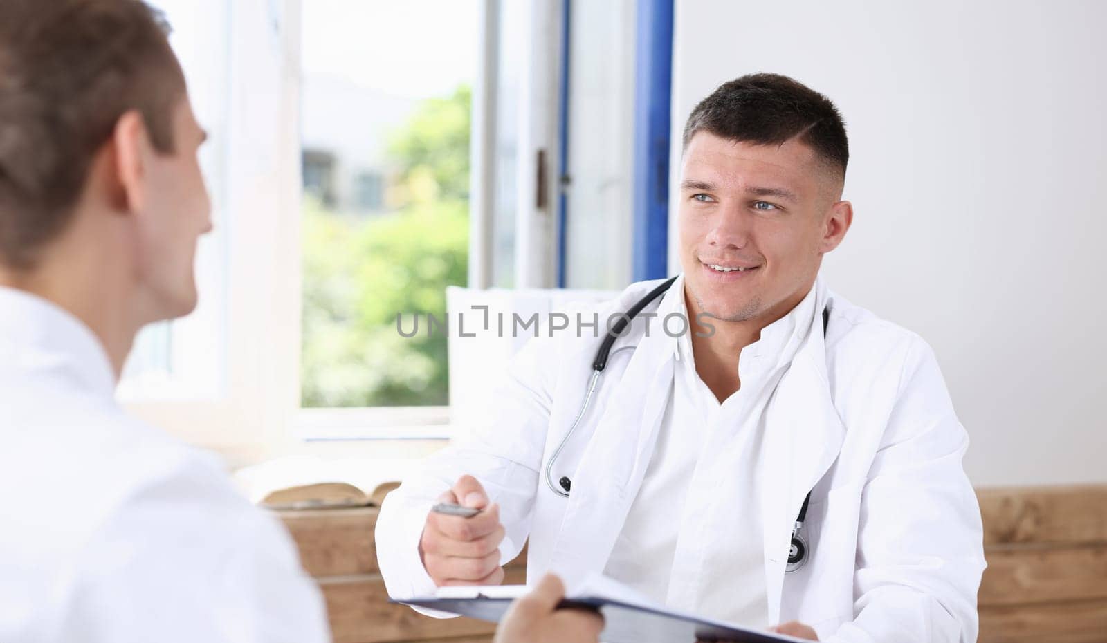 Concerned handsome doctor communicate with patient holding silver pen and showing pad. Physical agreement signature disease prevention consent sign 911 prescribe remedy healthy lifestyle concept