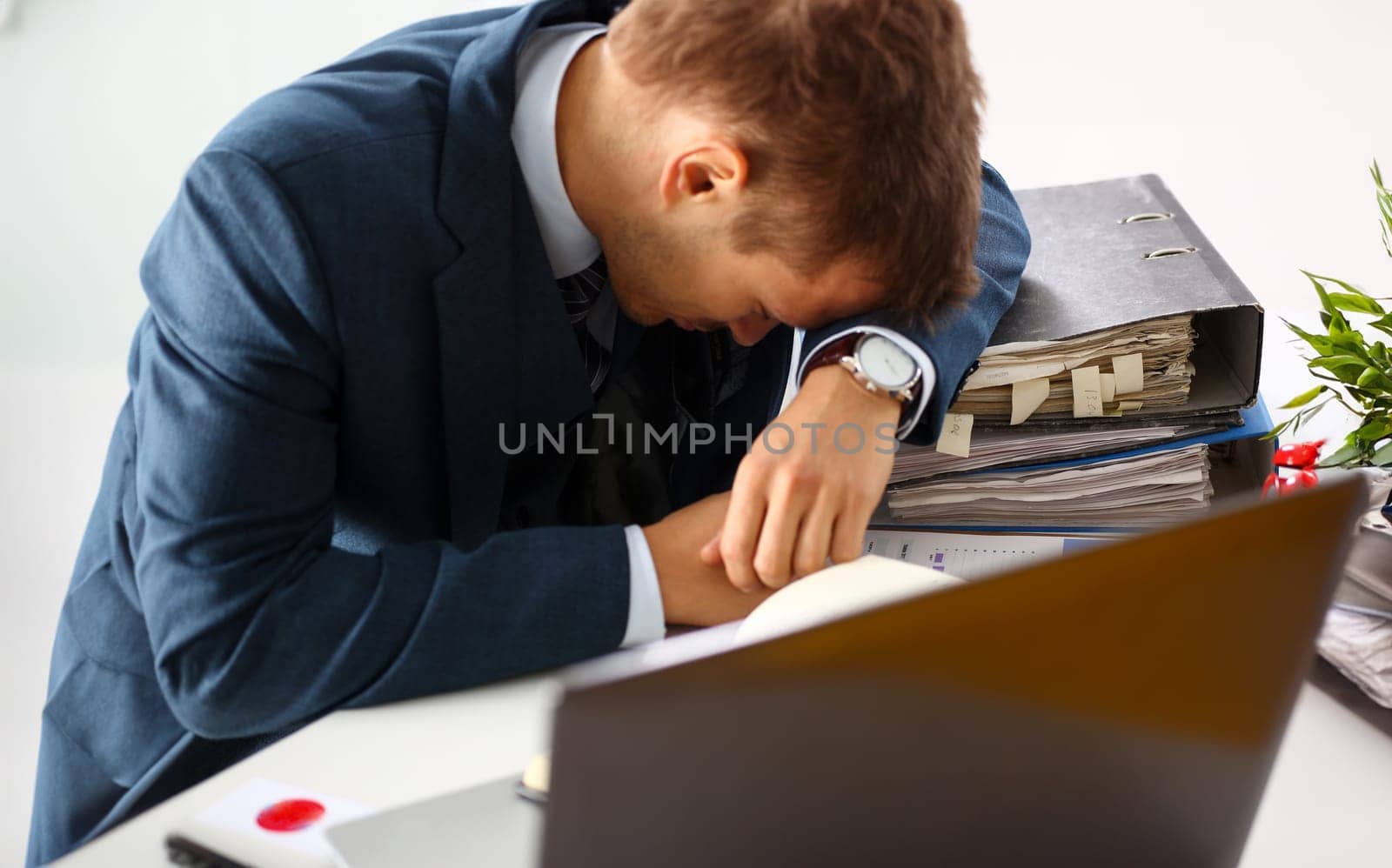 Tired office male clerk in suit take nap on table workplace full of exam papers. Sleepy white collar career frustration freelance employment fail study problem low energy down