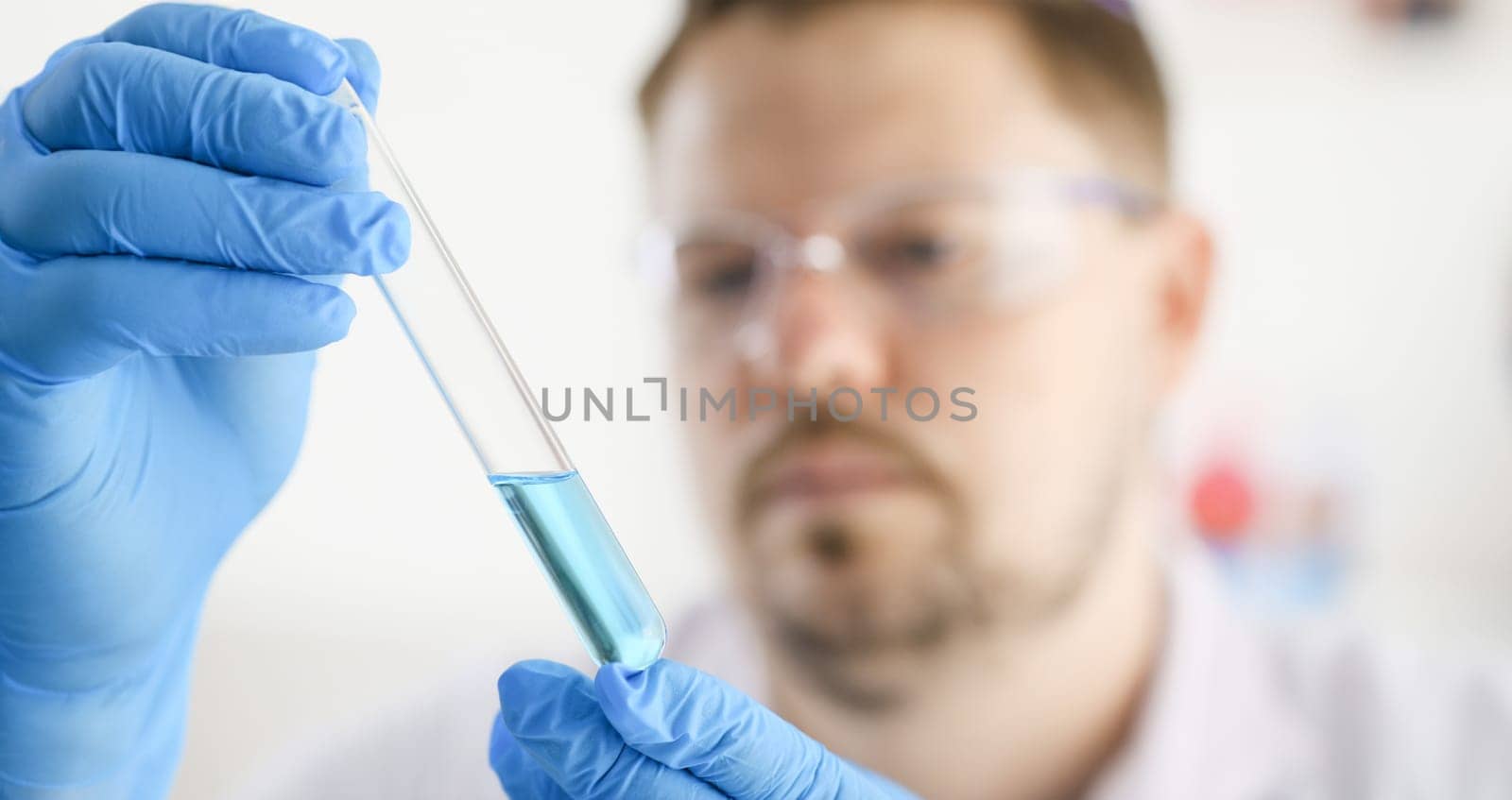 A male chemist holds test tube of glass in his hand overflows a liquid solution of potassium permanganate. Conducts an analysis reaction takes various versions of reagents using chemical manufacturing.