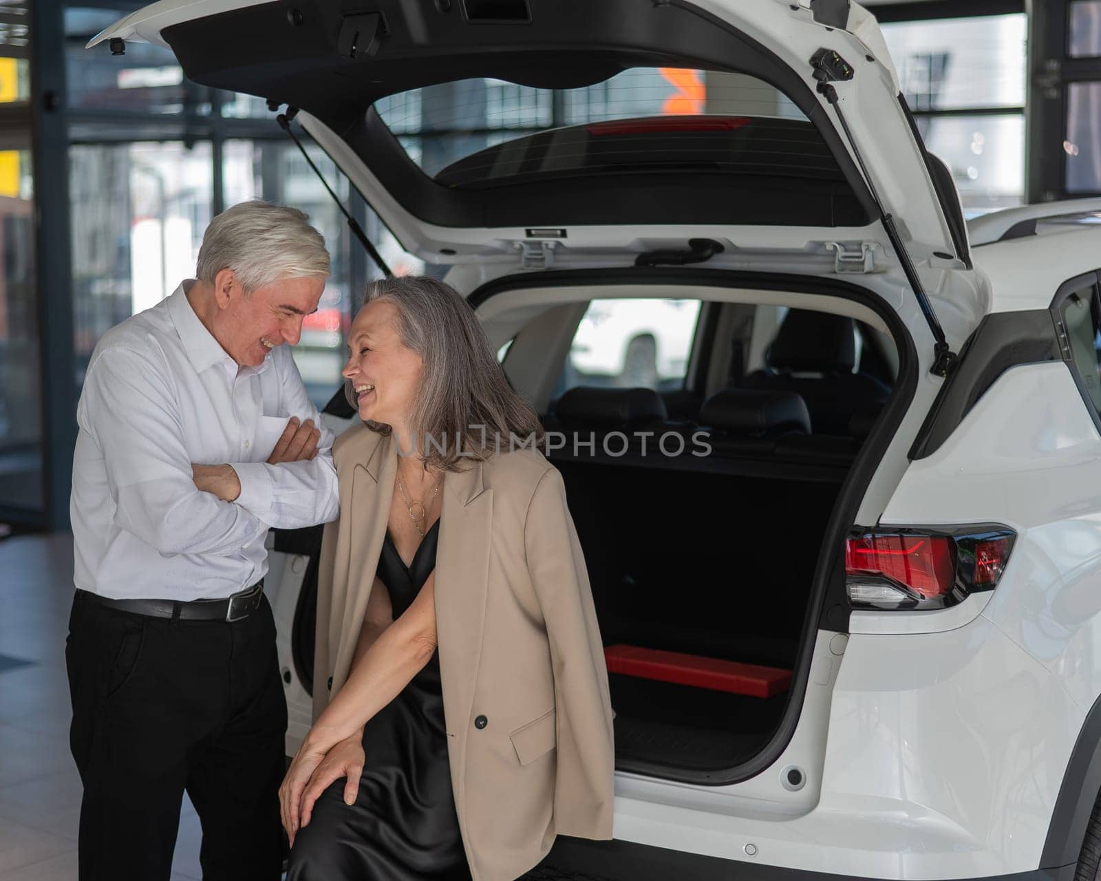 Mature Caucasian couple choosing a car looks at the trunk. by mrwed54