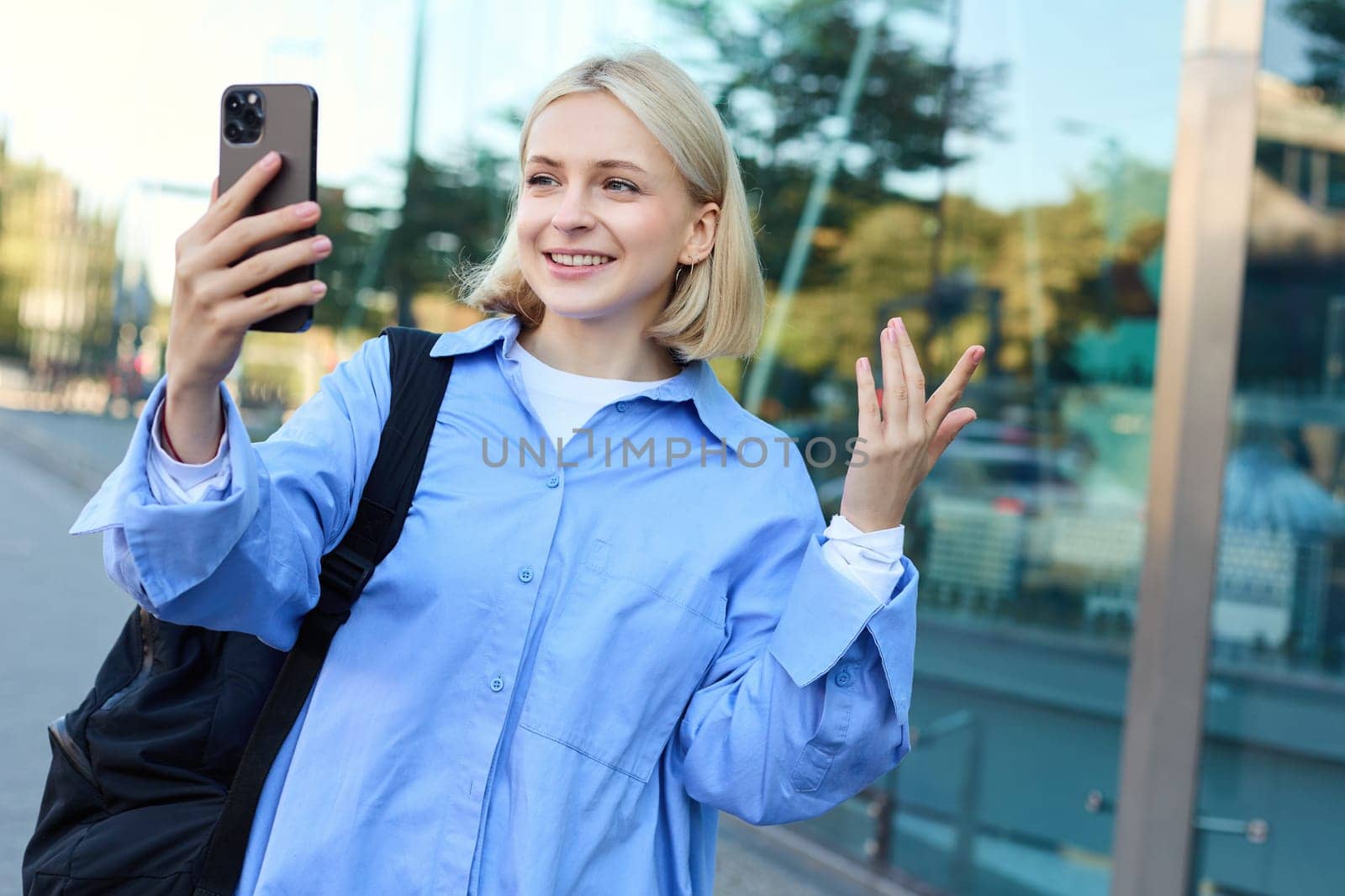 Portrait of smiling woman, lifestyle blogger recording video on smartphone, online chatting, looking at mobile camera, talking to someone online, standing on street.