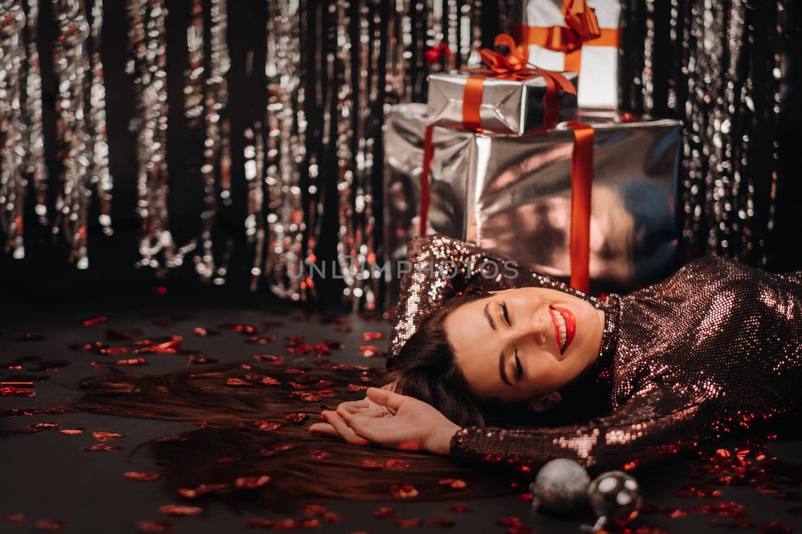 Top view of a girl lying in shiny clothes on the floor in confetti in the form of hearts and gifts.