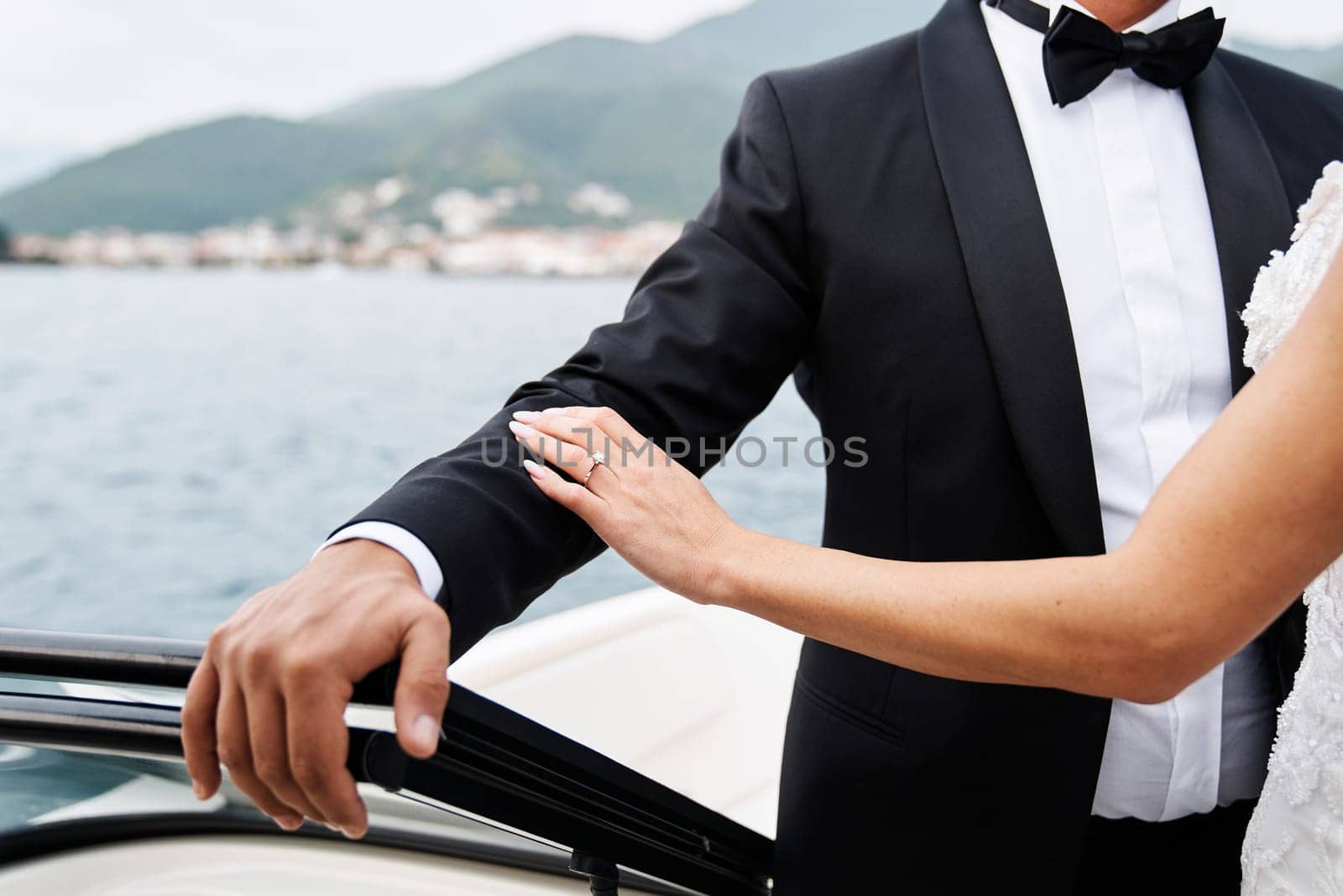 Bride touches groom hand while standing in a boat floating on the sea. Cropped. Faceless by Nadtochiy