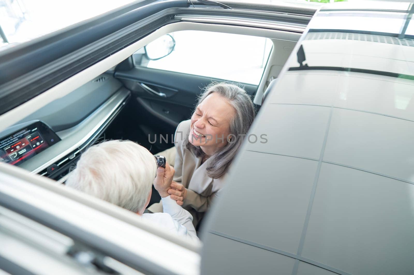 Mature Caucasian couple sitting in a new car and rejoicing at the purchase. Top view through the hatch