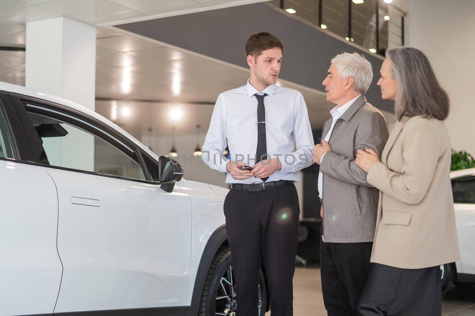 A salesman in a car dealership shows a car to a mature married couple