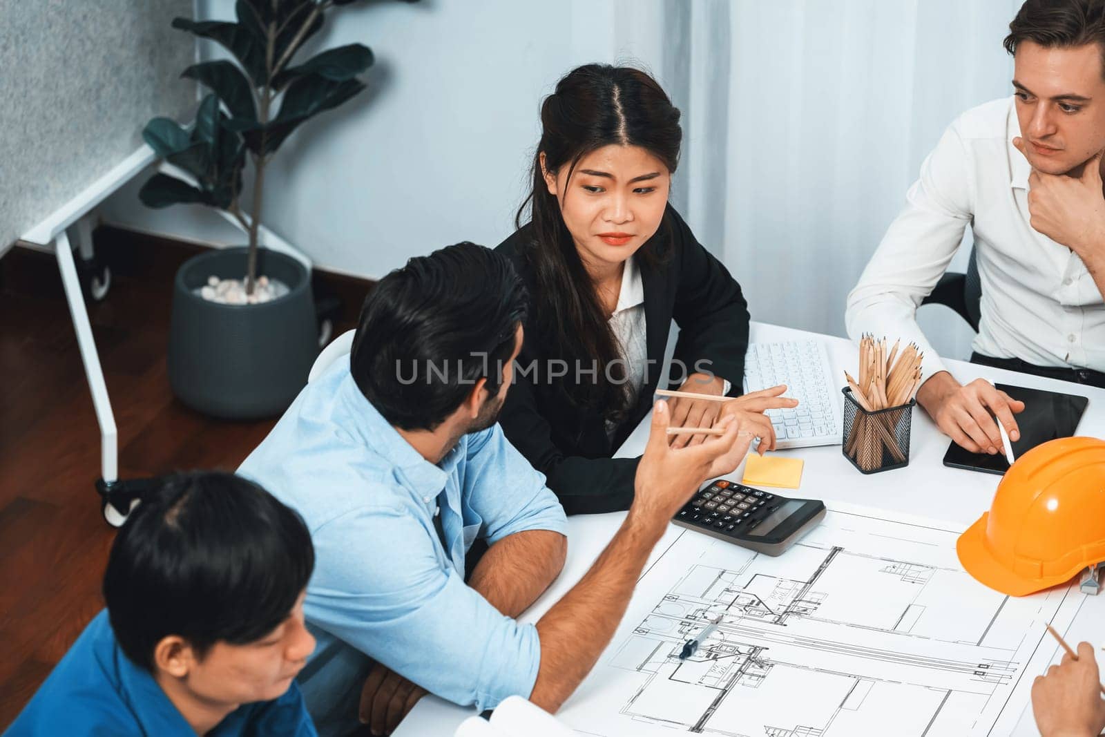 Diverse group of civil engineer and client working together on architectural project, reviewing construction plan and building blueprint at meeting table. Prudent