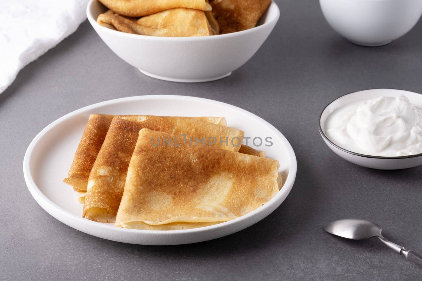 Plate with thin pancakes and sour cream on the table by NataliPopova