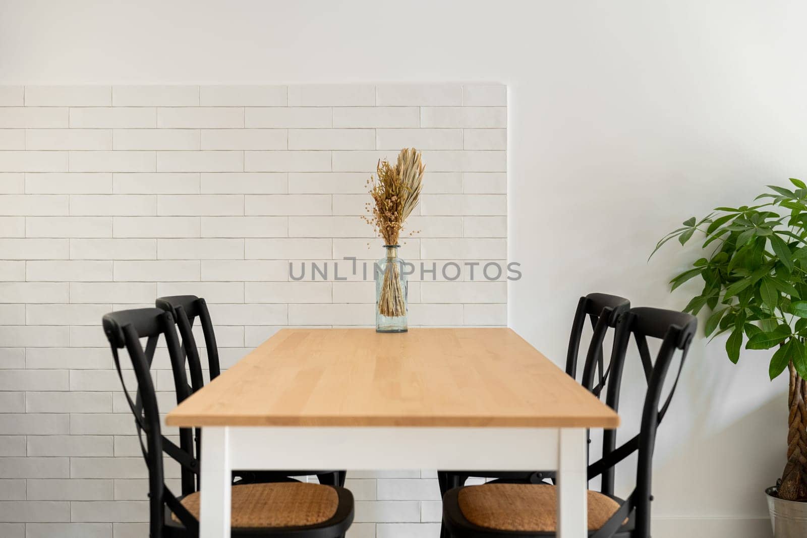 Wooden table with chairs and dry flowers bouquet in vase in dining room. Comfortable place to eat with modern furniture in domestic interior