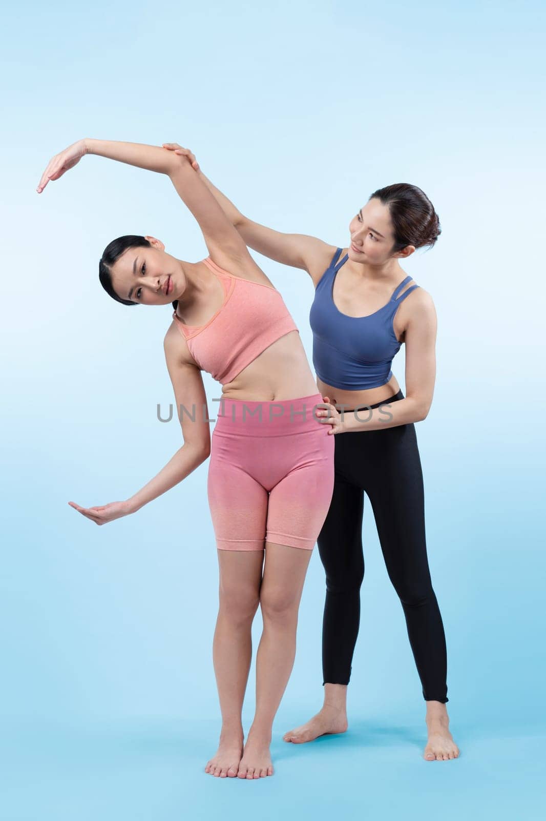 Asian woman in sportswear doing yoga exercise in standing pose with her trainer or yoga buddy. Healthy body care and meditation yoga lifestyle in full shot on isolated background. Vigorous