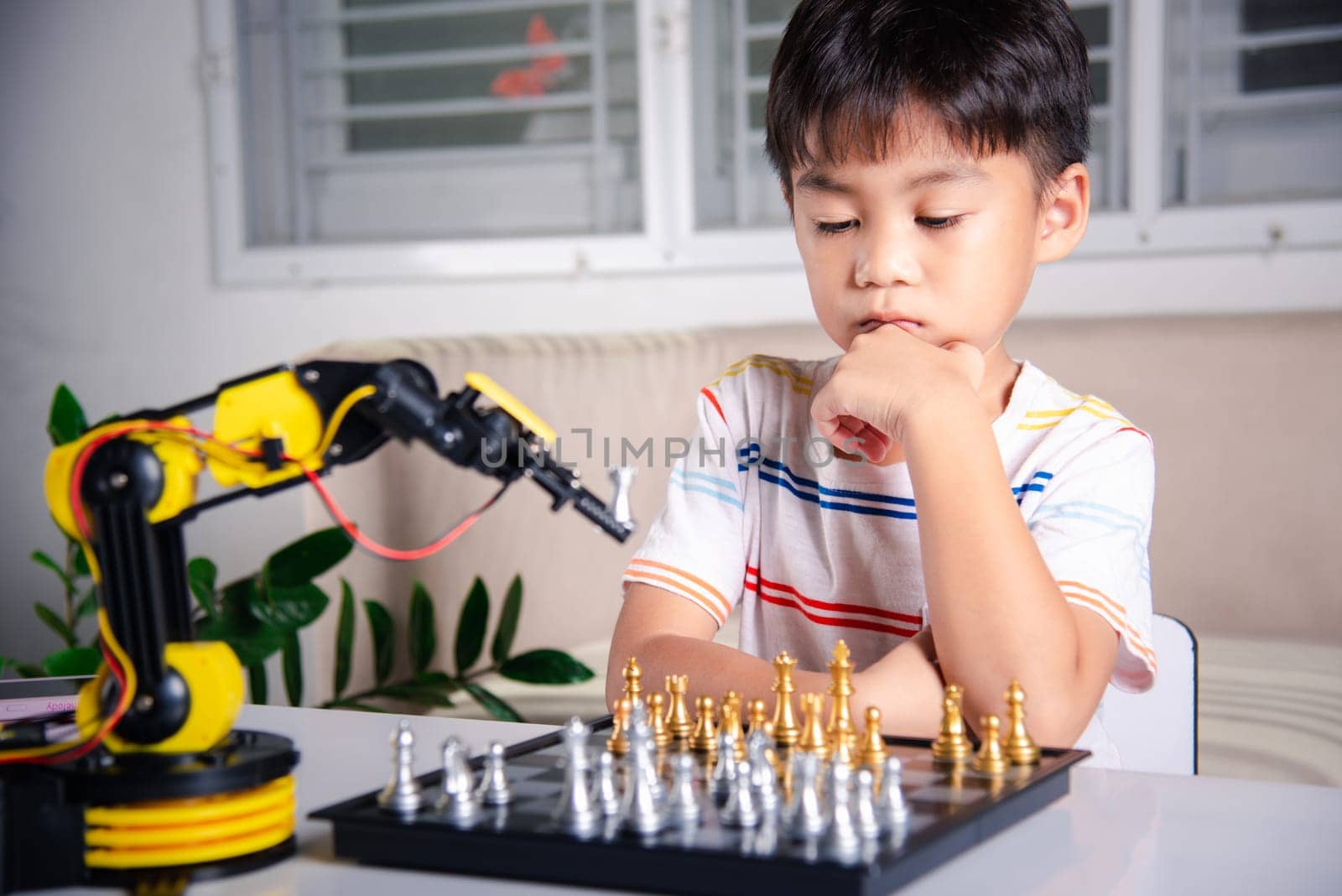 Asian little boy thinking and wait robot arm playing chess by Sorapop