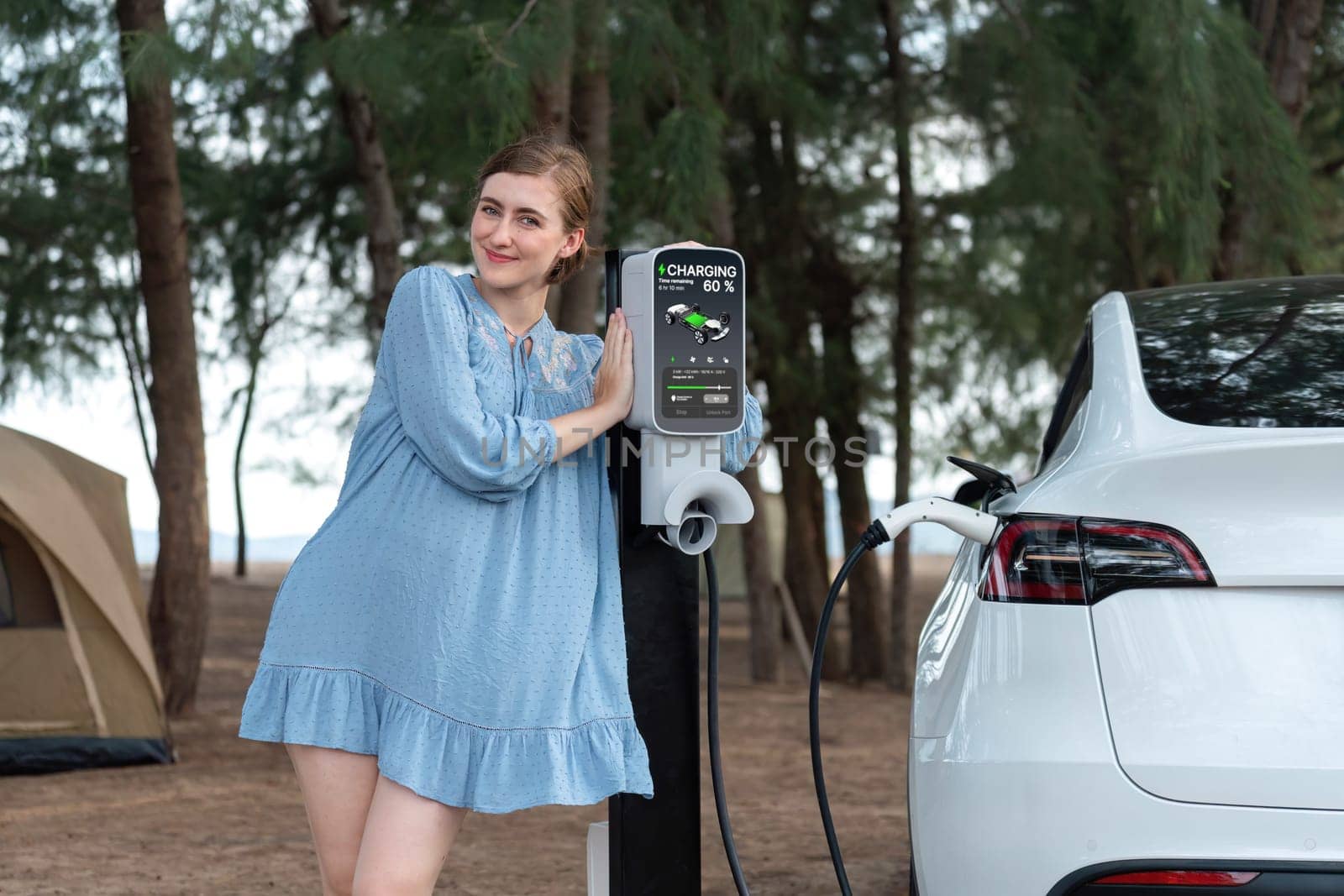 Holiday road trip vacation traveling to the beach camp with electric car, young woman recharge EV vehicle with green and clean energy. Beach travel camping with eco-friendly EV car .Perpetual