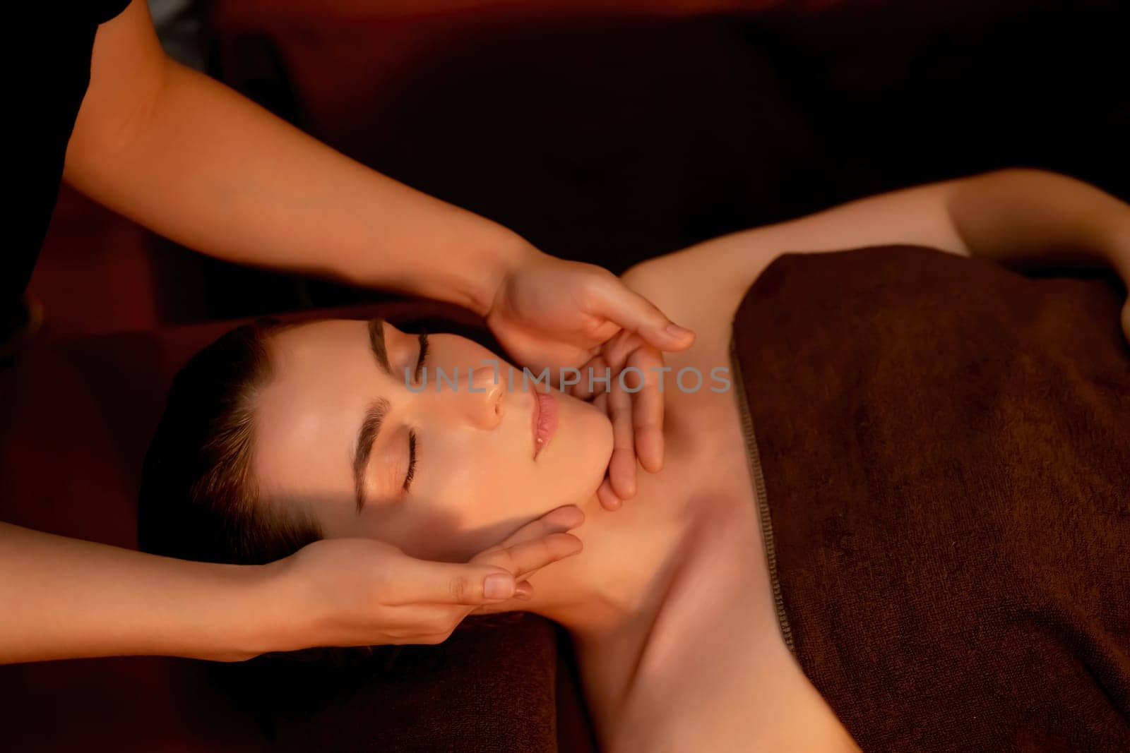 Caucasian woman enjoying relaxing anti-stress head massage and pampering facial beauty skin recreation leisure in warm candle lighting ambient salon spa in luxury resort or hotel. Quiescent