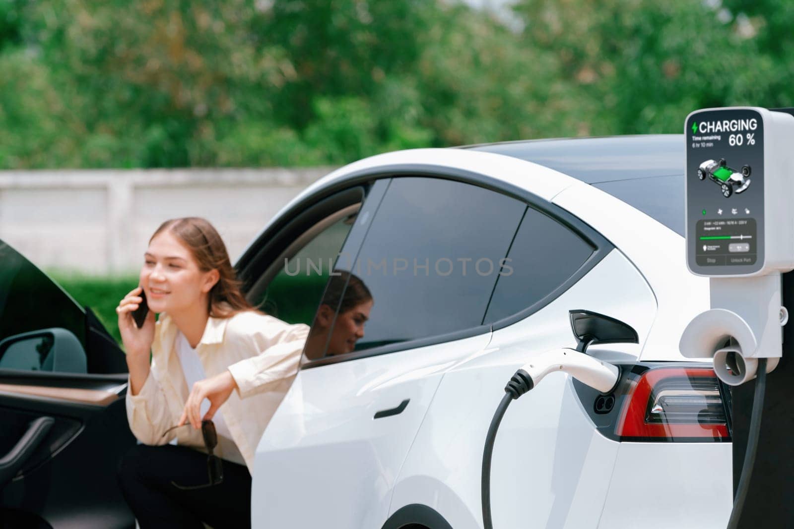 Young woman recharge her EV electric vehicle at green city park. Expedient by biancoblue