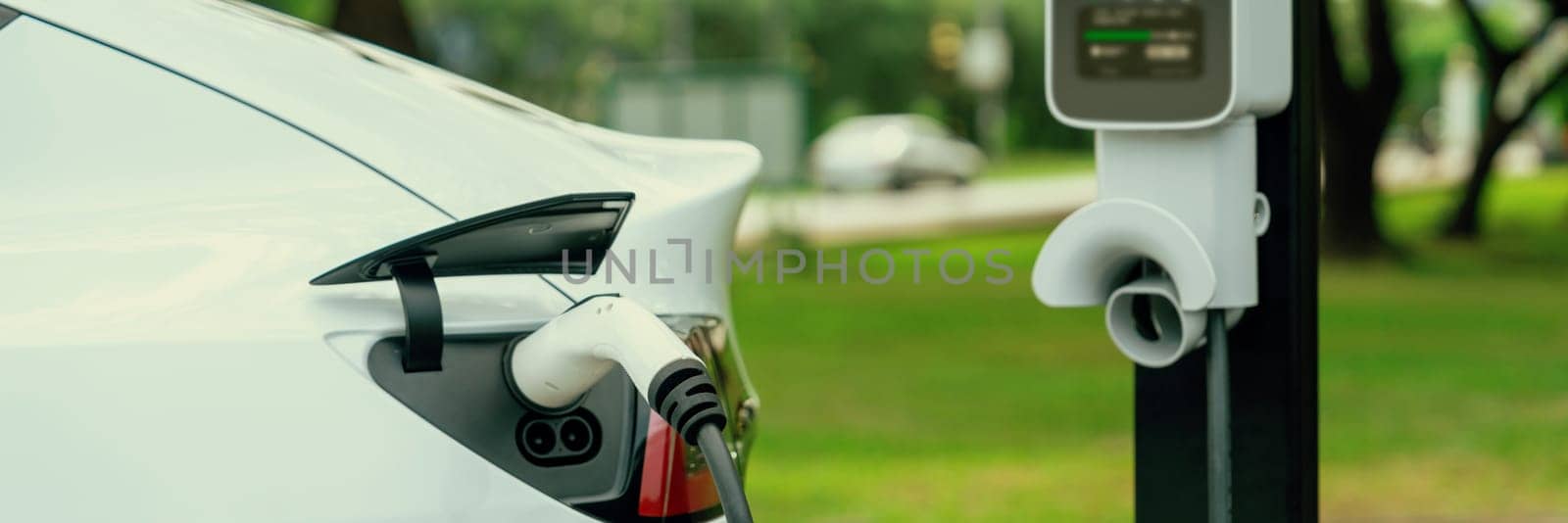 EV vehicle recharging from EV charging station in green city park Exalt by biancoblue