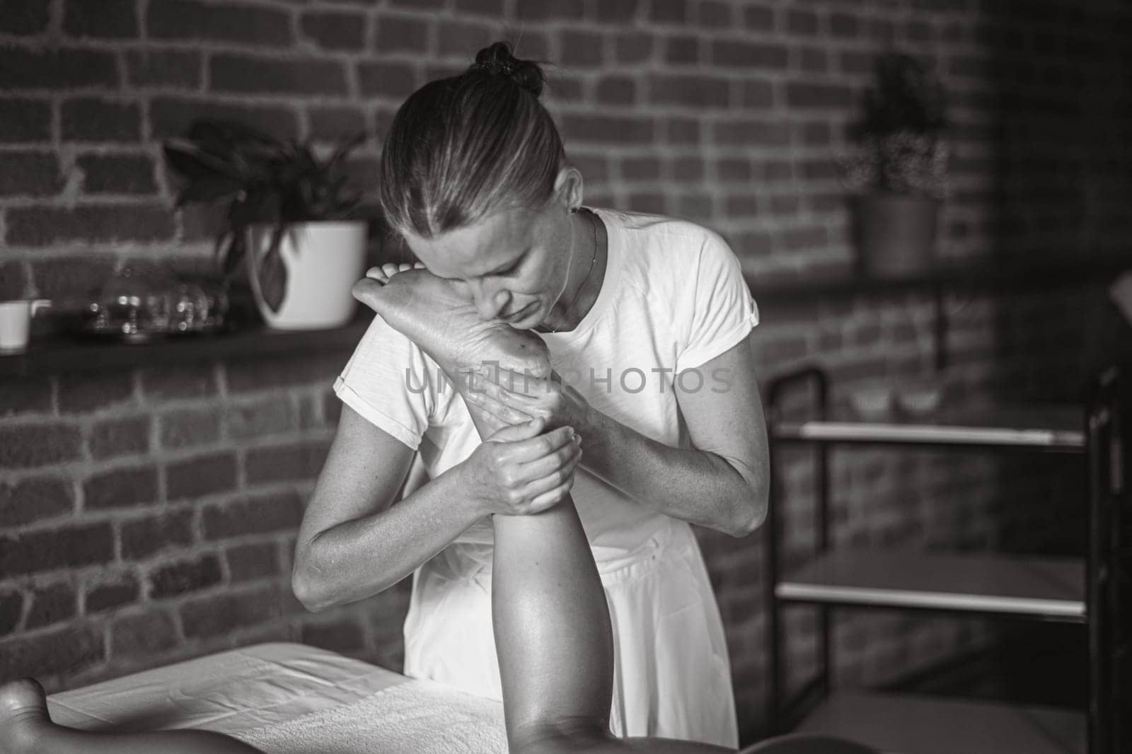 professional caucasian female physiotherapist masseuse performing leg massage to hispanic latino brunette woman in spa clinic