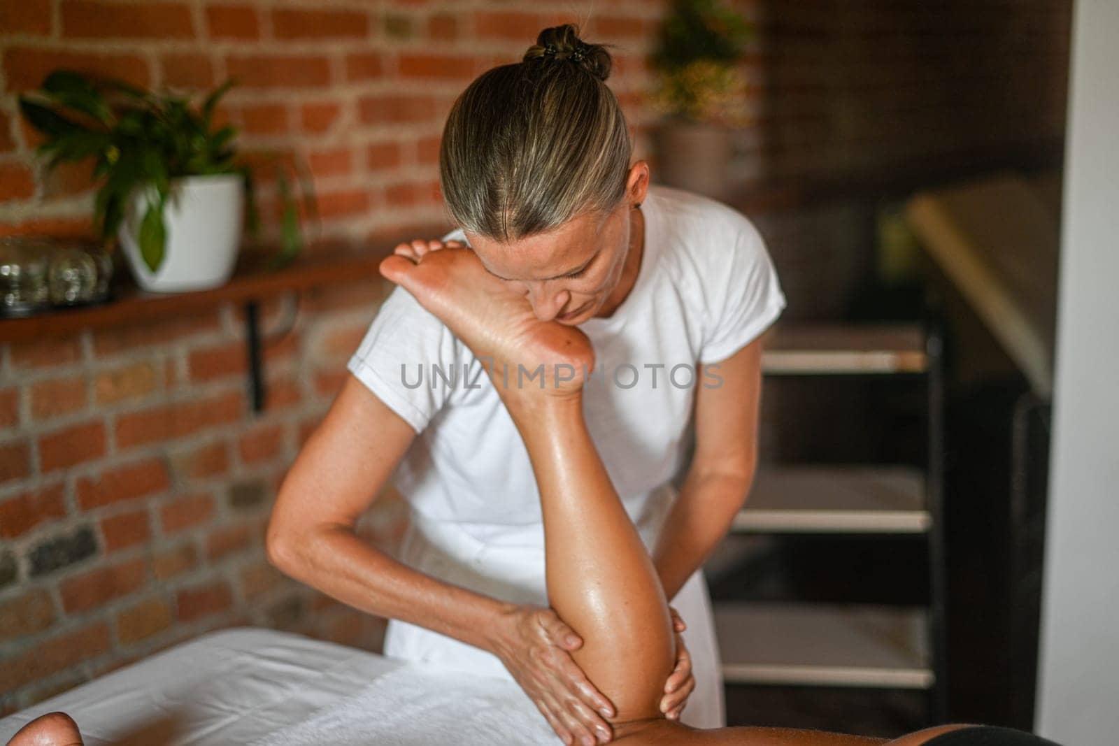 professional female physiotherapist masseuse performing leg massage to hispanic woman in spa clinic by verbano