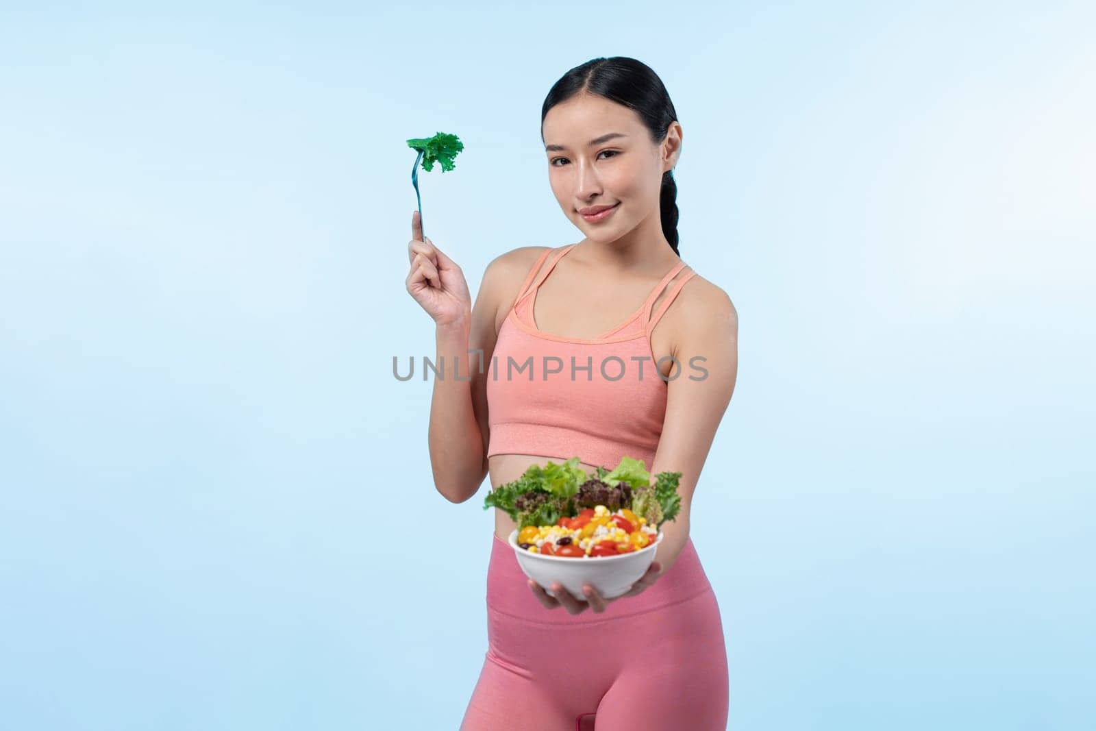 Young sporty Asian woman in sportswear holding salad bowl fill with vibrant of fruit and vegetable. Natural youthful and fit body lifestyle with balance nutrition on isolated background. Vigorous