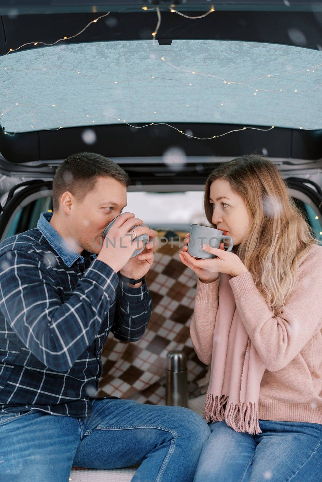 Man and woman drink coffee from cups while sitting opposite each other in the trunk of a car. High quality photo