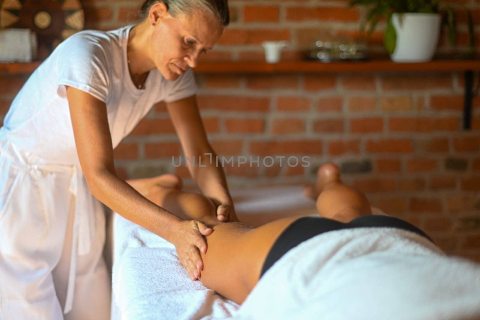 professional female physiotherapist masseuse performing leg massage to hispanic woman in spa clinic by verbano