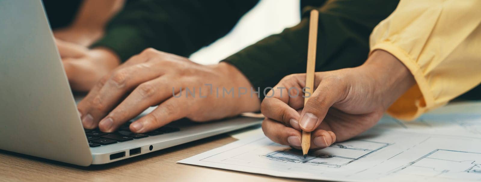 A portrait of skilled architect engineer hand writing a detail of blueprint during male engineer searching data from laptop at modern architectural office. Focus on hand. Closeup. Delineation.