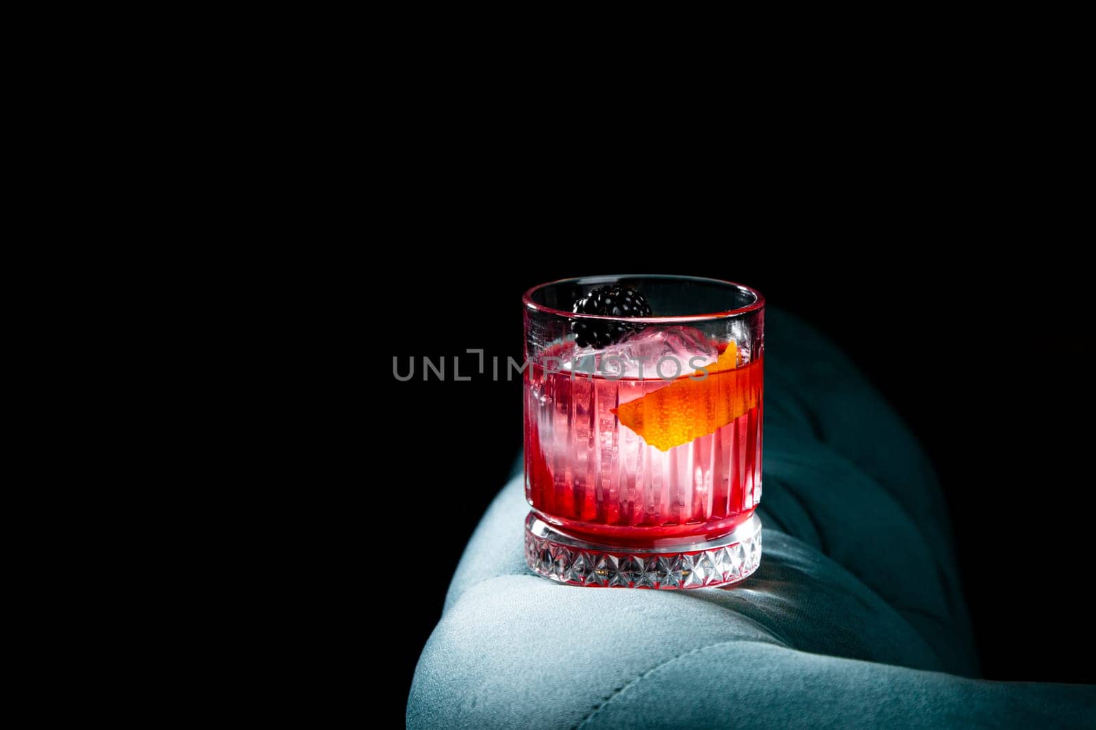 red cocktail in a transparent glass with round ice, whipped cream and black berry on top