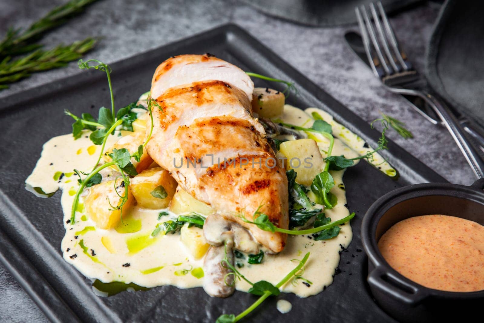 side view of chicken breast in cheese sauce with herbs on a black tray. High quality photo