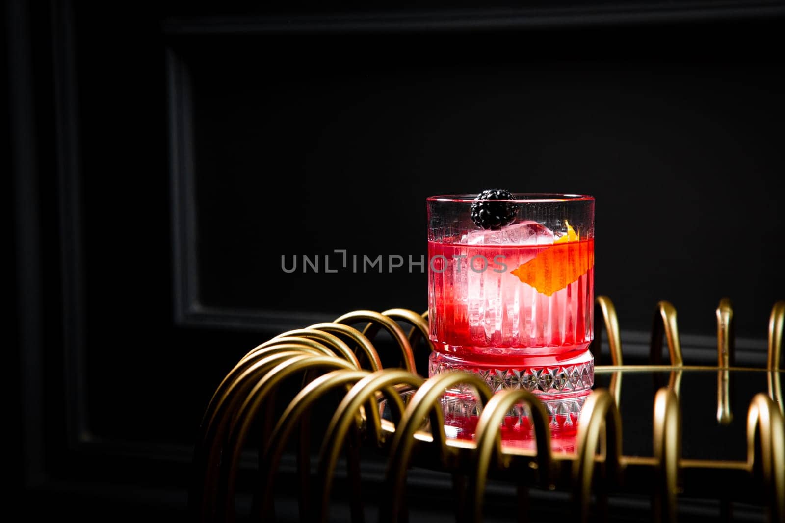 red cocktail in a transparent glass with round ice, whipped cream and black berry on top