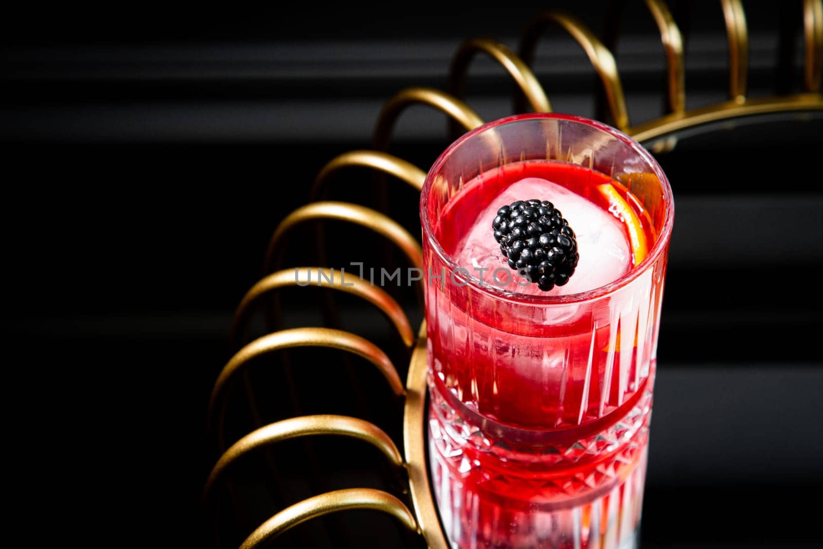 red cocktail in a transparent glass with round ice, whipped cream and black berry on top