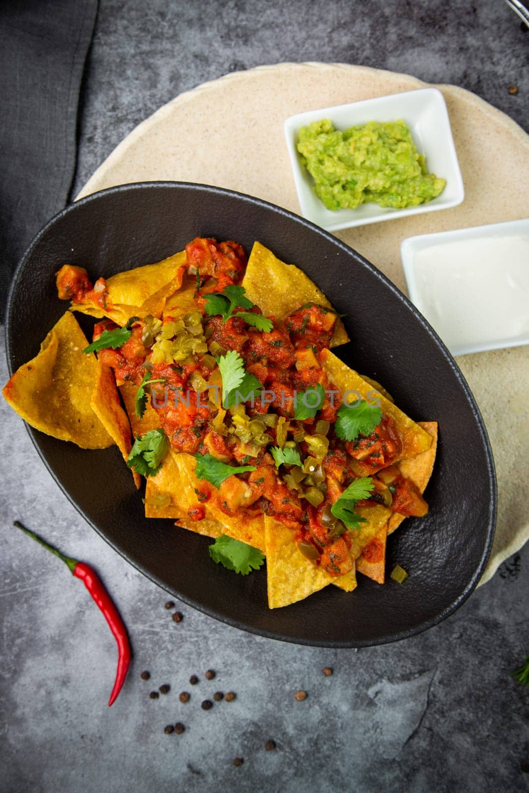 nachos with sauce, meat and herbs in a black plate