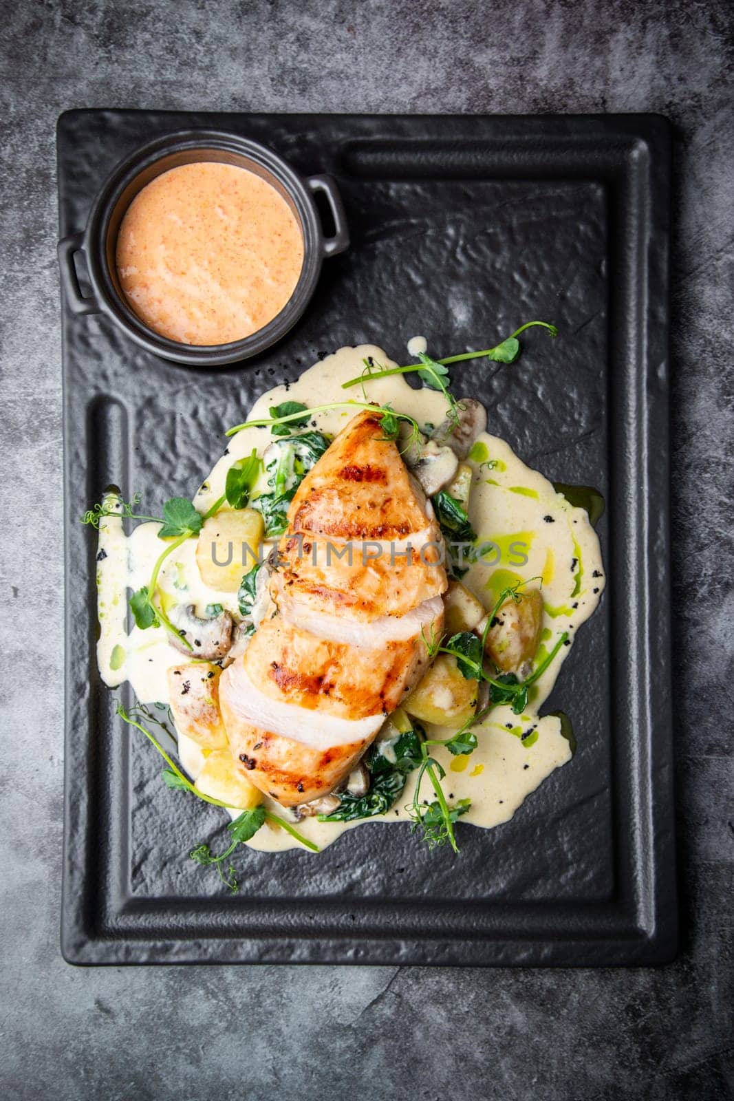 side view of chicken breast in cheese sauce with herbs on a black tray. High quality photo