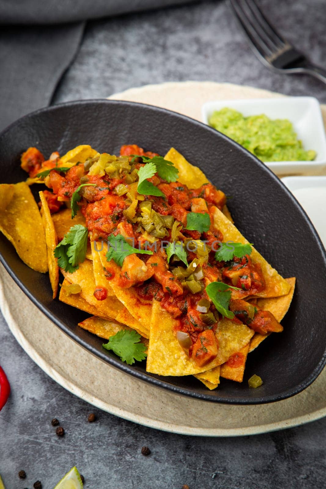 nachos with sauce, meat and herbs in a black plate