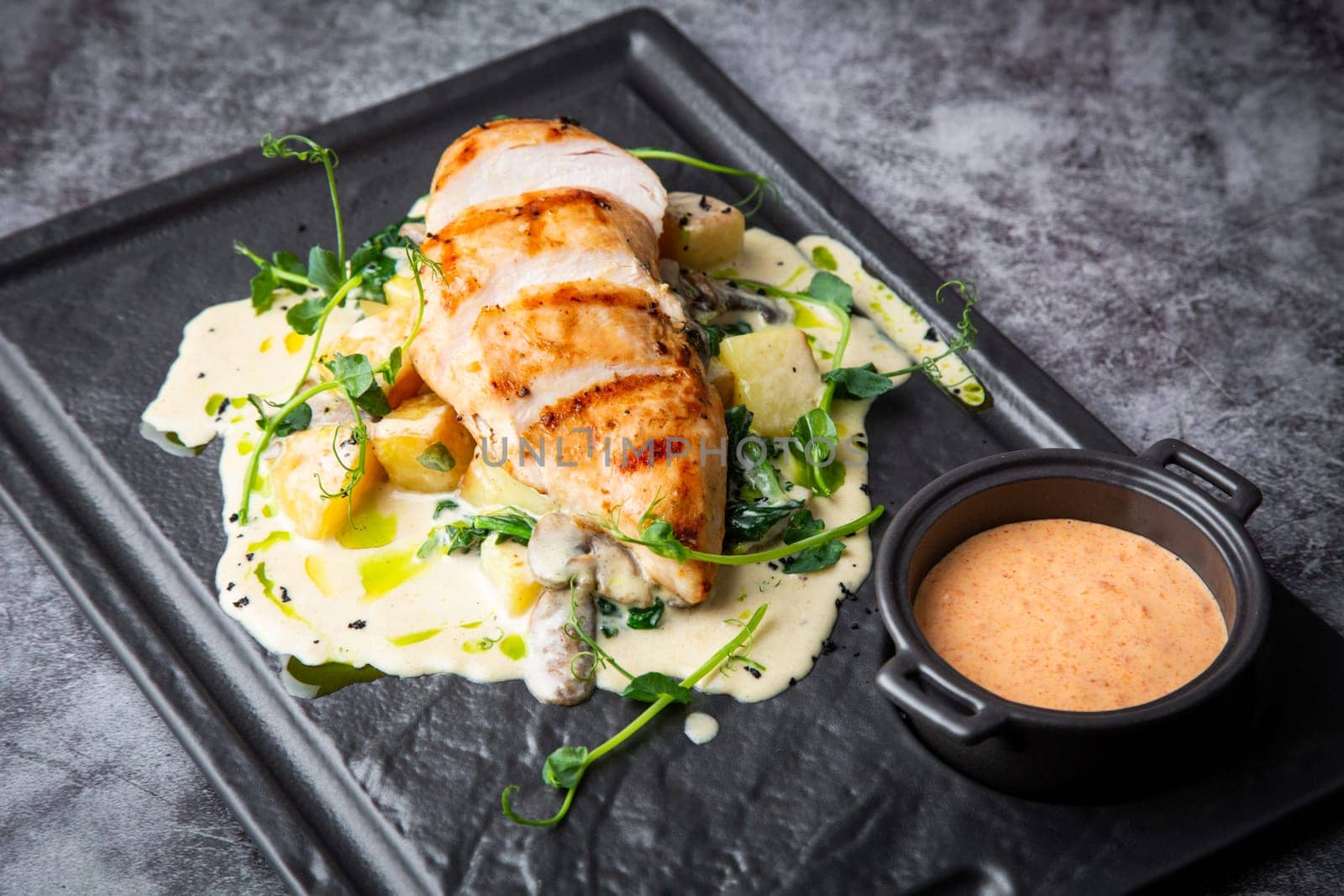 side view of chicken breast in cheese sauce with herbs on a black tray. High quality photo