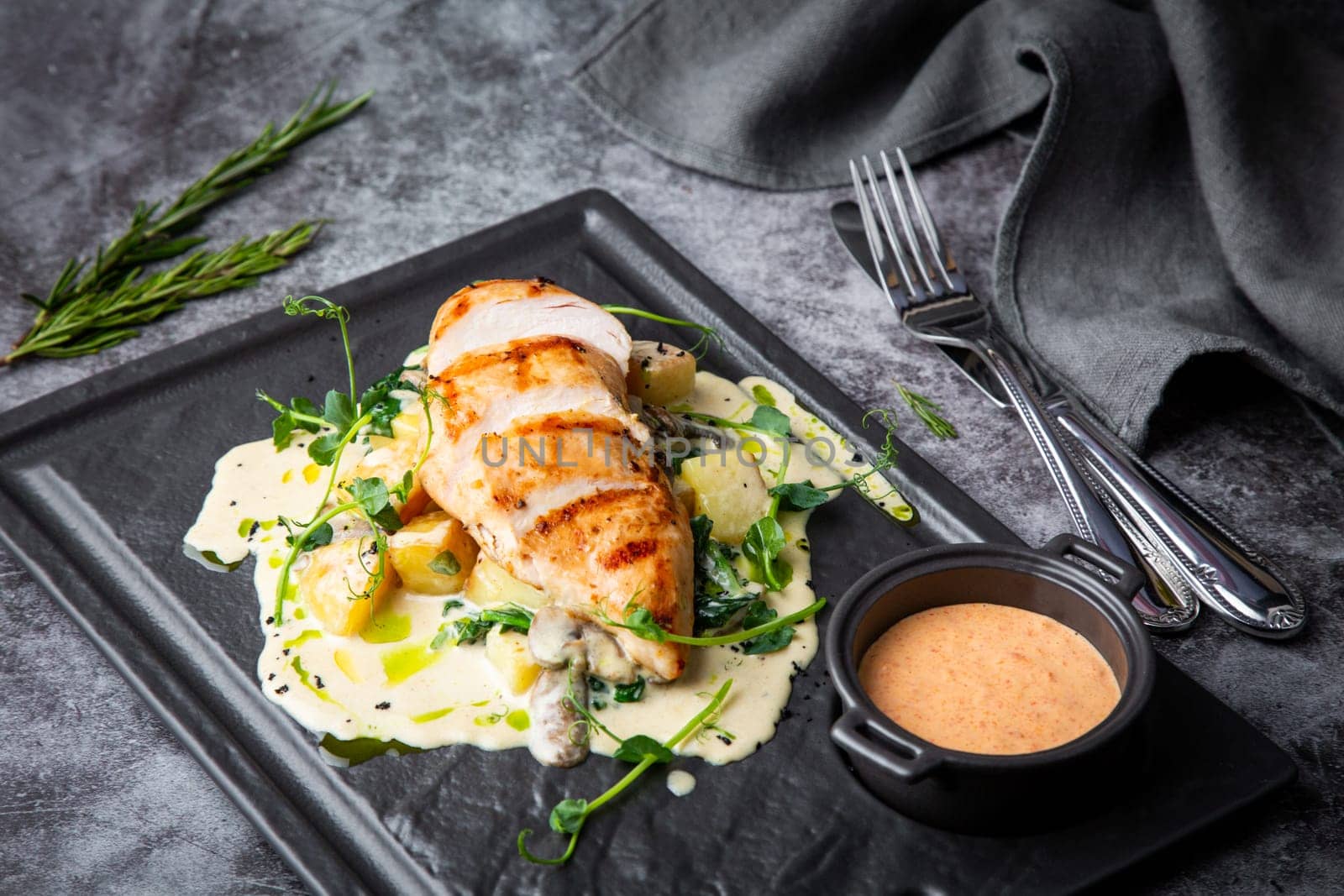 side view of chicken breast in cheese sauce with herbs on a black tray. High quality photo