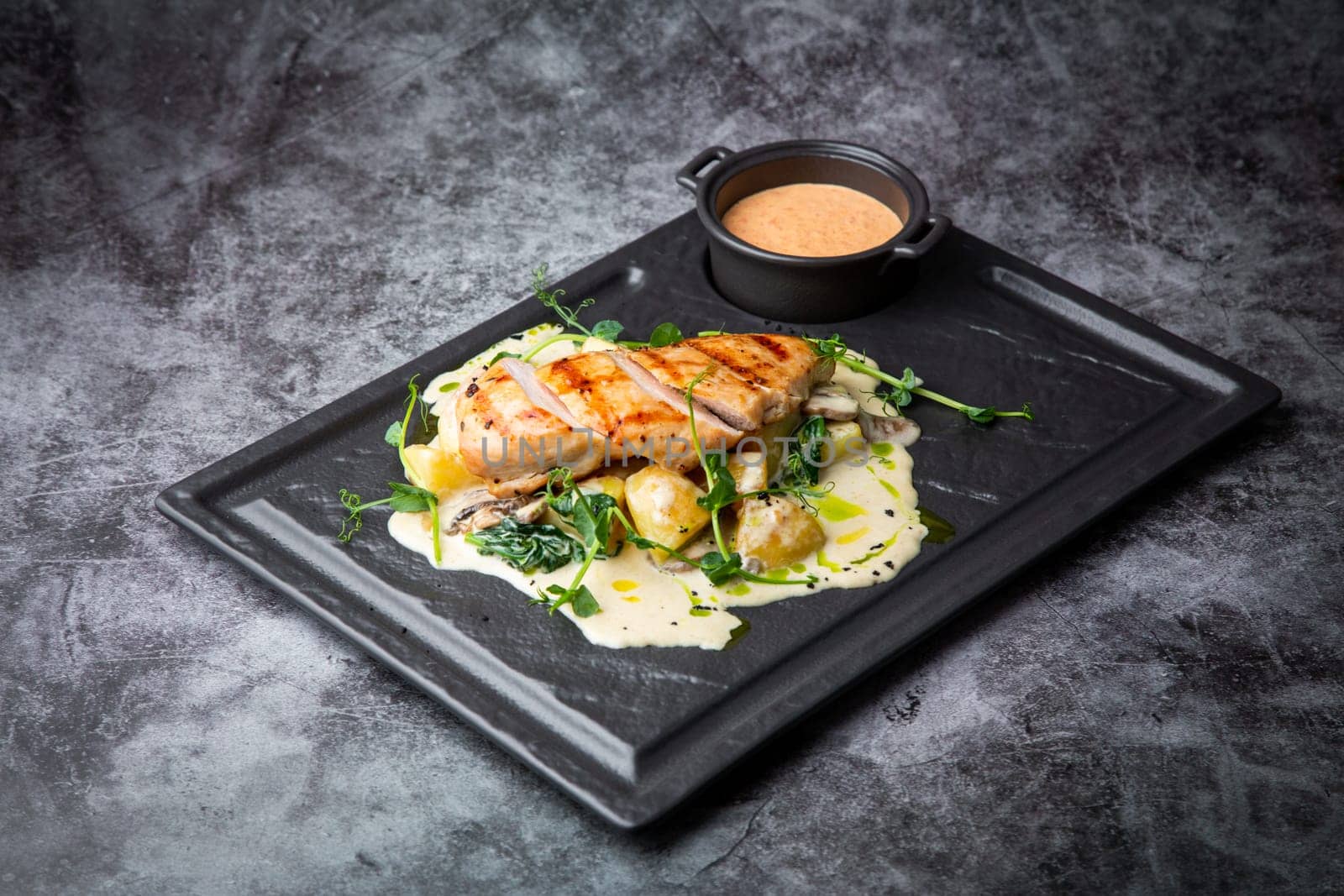 side view of chicken breast in cheese sauce with herbs on a black tray. High quality photo