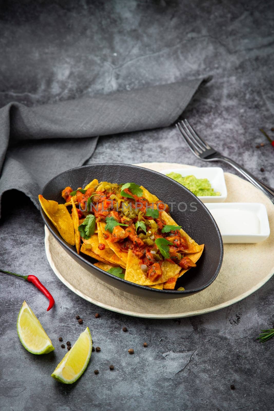 nachos with sauce, meat and herbs in a black plate, side view by tewolf